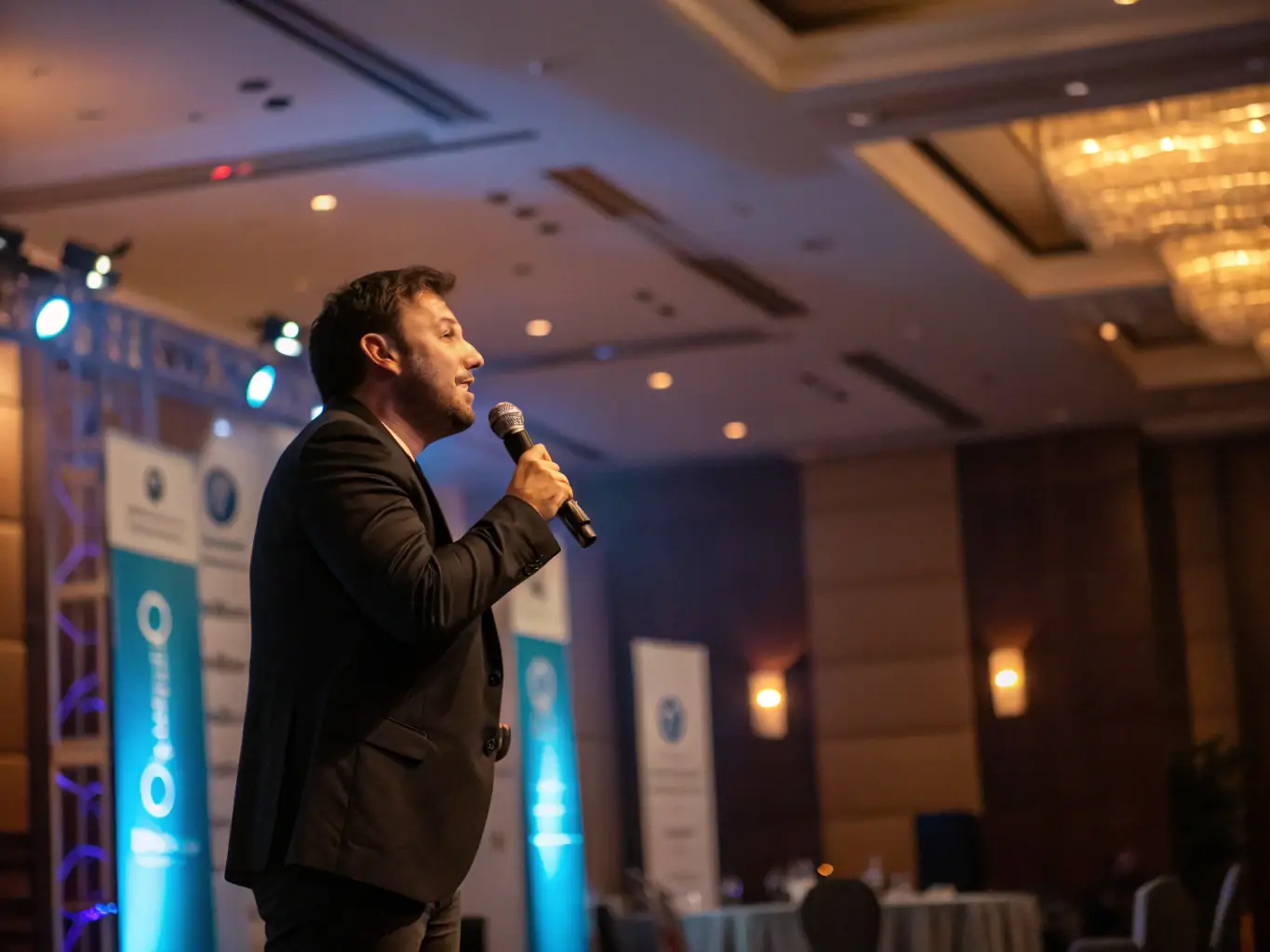 A confident individual delivering a speech on stage, bathed in warm lighting, showcasing effective public speaking skills in a professional setting. The audience is engaged and attentive, reflecting the impact of clear communication.